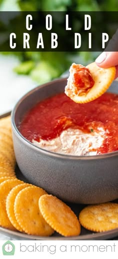 a hand dipping some crackers into a bowl of dip with cheese and tomato sauce