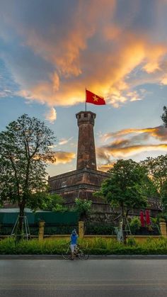 a person riding a bike past a tall tower with a flag on it's top