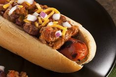 a hot dog with onions, cheese and chili on it's bun sitting on a black plate