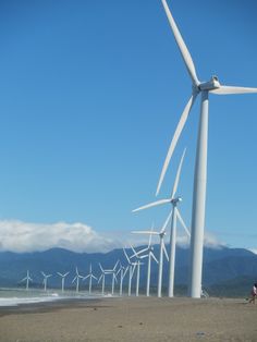 a group of people standing on top of a sandy beach next to wind turbine turbines