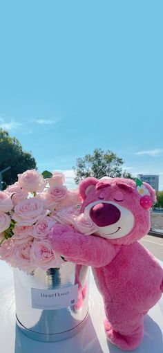 a pink teddy bear sitting on top of a table next to a bouquet of flowers