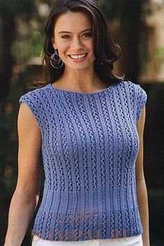 a woman wearing a blue knitted sweater and white pants smiles at the camera while walking