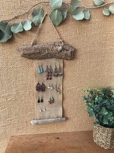 a wall hanging with earrings on it next to a potted plant and wooden table