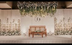 a wooden bench sitting in front of a white wall with flowers and greenery on it