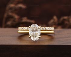 an oval cut diamond ring on top of a wooden surface with diamonds around it and gold band