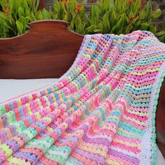 a multicolored crocheted blanket sitting on top of a wooden bench next to potted plants