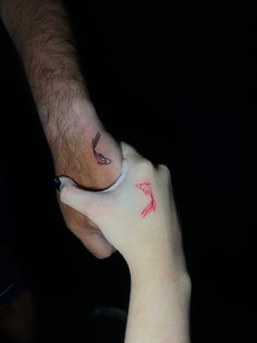 two people holding each other's hands with red ink on their fingers and one has a bird tattoo on it