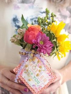 a woman holding a vase with flowers in it and a gift wrapped in a card