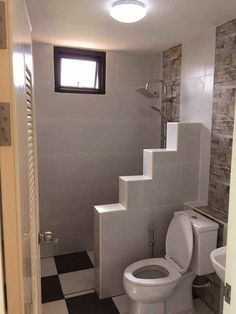 a white toilet sitting under a window next to a sink in a bathroom with tiled walls