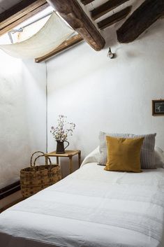 a white bed sitting under a wooden beam in a bedroom next to a table with flowers on it