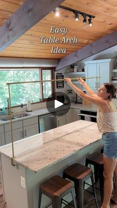 a woman standing on top of a kitchen counter next to an island with stools