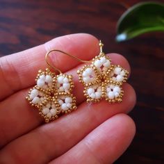 a pair of white beaded earrings sitting on top of a wooden table next to a plant