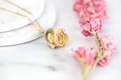 two necklaces with pink flowers on them sitting next to some white plates and silverware