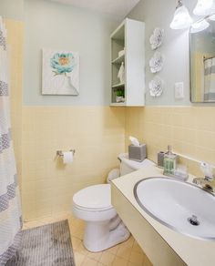 a white toilet sitting next to a sink in a bathroom under a mirror and shower curtain