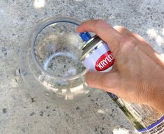 a hand holding a can of kryle on top of a glass bowl filled with water