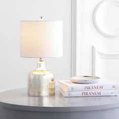 a lamp sitting on top of a table next to two books and a glass vase