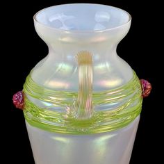 a white vase with green and pink trimmings on the bottom, sitting in front of a black background