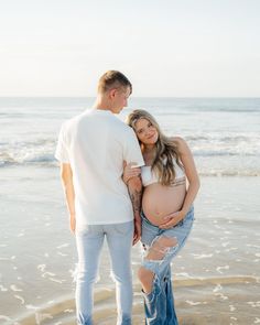 a pregnant couple standing on the beach with their belly wrapped around each other's waist