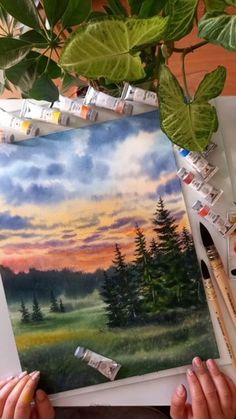 someone is working on a painting with paintbrushes and watercolors in front of them