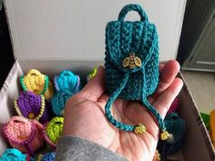 a hand holding a small crocheted purse in it's left hand, surrounded by other crocheted items