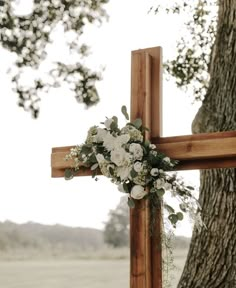 a cross decorated with flowers and greenery next to a tree in front of a field