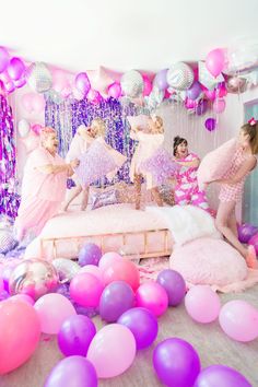 a group of women dressed in pink and purple dancing on a bed surrounded by balloons