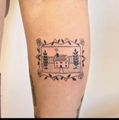 a tattoo on the leg of a person with a frame around it that has an image of a house and trees