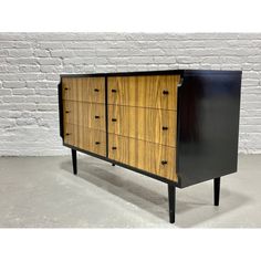 a black and wood dresser with drawers on it's sides, against a white brick wall