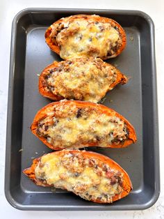 four stuffed sweet potatoes in a baking pan with cheese on top and other toppings