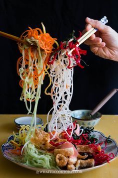 someone is holding chopsticks over a plate of food with noodles and vegetables on it