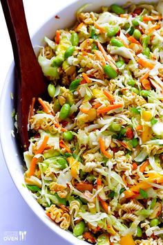 a white bowl filled with rice and vegetables next to a wooden serving utensil