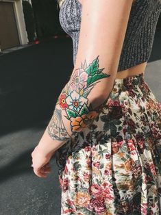 a woman with a flower tattoo on her arm is walking down the street while wearing a skirt