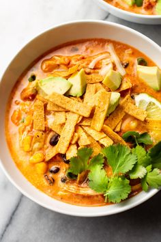 two bowls of soup with tortilla chips and avocado garnish