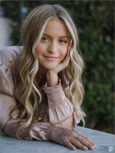 a woman with long blonde hair is leaning on a table and looking at the camera