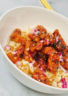 a white bowl filled with rice and meat on top of a table next to chopsticks