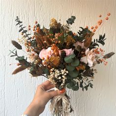 a person holding a bouquet of flowers in front of a white wall with orange berries