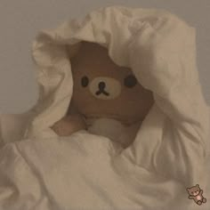 a brown teddy bear peeking out from under a white comforter on a bed with pillows