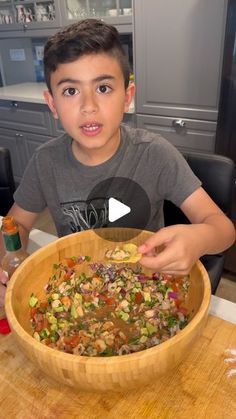 a young boy holding a wooden bowl filled with vegetables