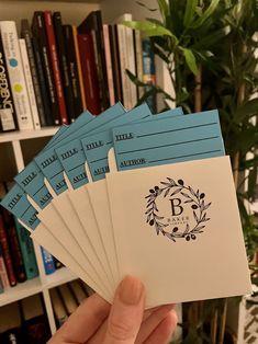 a person holding up six envelopes in front of a bookshelf