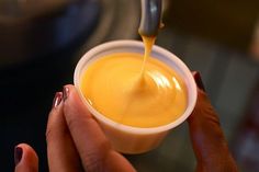 a person holding a small cup filled with orange liquid and sauce being poured into it