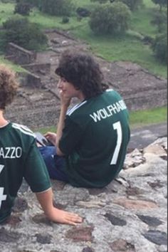 two young boys sitting on top of a rock next to each other and looking at something