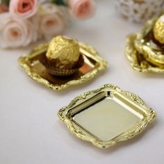 three small gold trays with cupcakes on them and flowers in the background