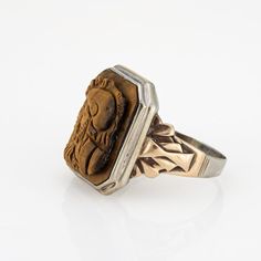 This is part of Chairish’s Fine Jewelry assortment.  Finely detailed vintage Art Deco era tigers eye cameo ring crafted in 10 karat white & yellow gold (circa 1920s to 1930s).   Tigers eye measures 16mm x 12mm. The tiger's eye is in good condition (few very minor chips visible under a 10x loupe).   The tigers eye cameo depicts the side profile of two Centurions. The tiger's eye is luminous with warm golden hues visible with every movement of the ring. The square mount has a low profile and rises Antique Carved Collectible Ring, Antique Brown Ring Jewelry, Vintage Carved Signet Ring, Vintage Carved Signet Ring Collectible, Antique Brown Carved Jewelry, Victorian Style Brown Collectible Jewelry, Victorian Brown Collectible Jewelry, Antique Brown Cabochon Ring, Gold Coin Ring