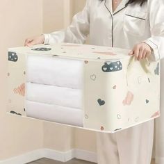 a woman in pajamas is holding a box with sheets on it and the lid opened