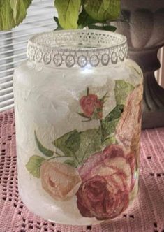 a vase with flowers painted on it sitting on a doily next to a potted plant