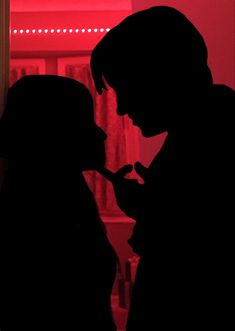 a man and woman are silhouetted against a red background in front of a window