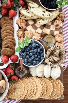 a platter filled with crackers, berries and cookies