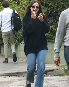 a woman in black sweater and jeans walking down the street with her hand on her mouth