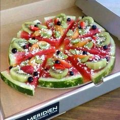 a pizza with many different types of fruits on it in a box, ready to be eaten