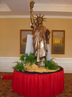 the statue of liberty is on top of a red tablecloth in front of two framed pictures